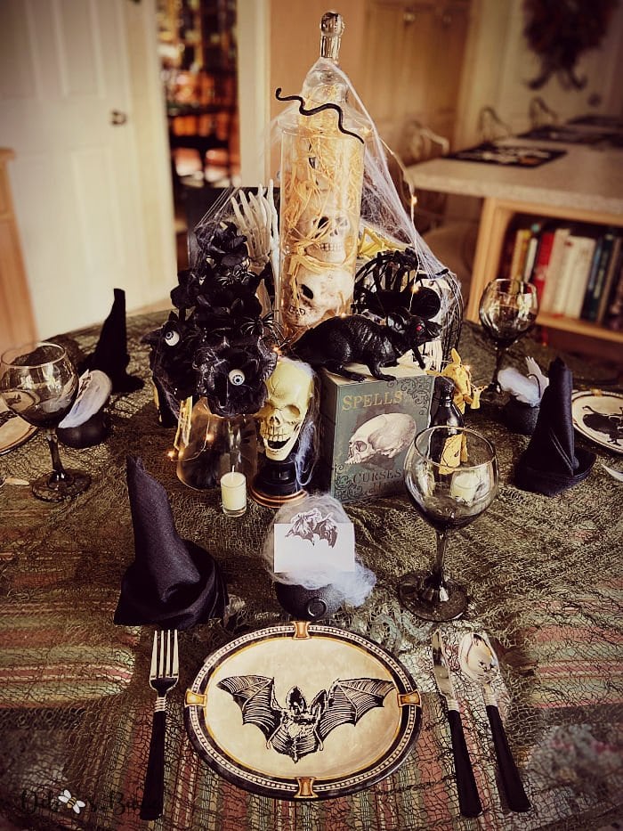 A very spooky Halloween centerpiece and table decor including skulls, webs, a spell book, large rat all cloistered togetjer in the middle of the table