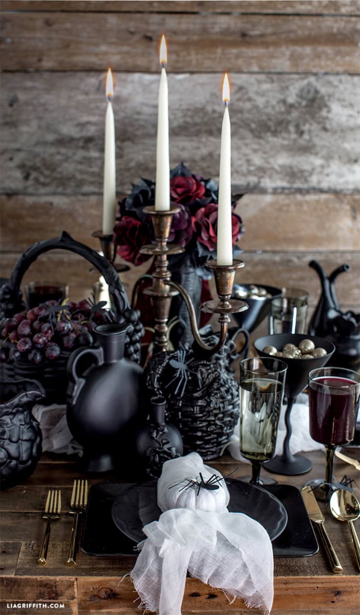An elegant black tablesetting with a elaborate Halloween centerpiece featuring candelabras, spiders and black apothecary jars.