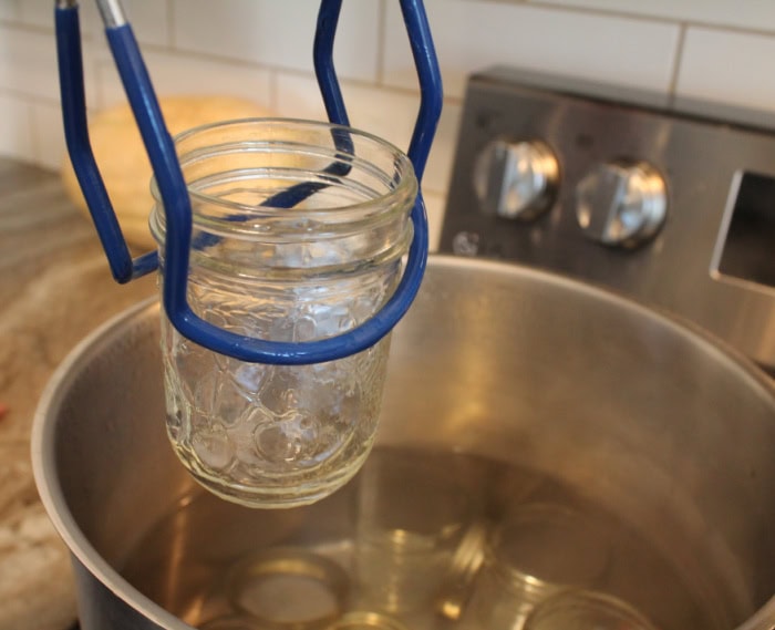 Lifting a sterile jar using a jar lifter while making a saskatoon berry jam recipe.