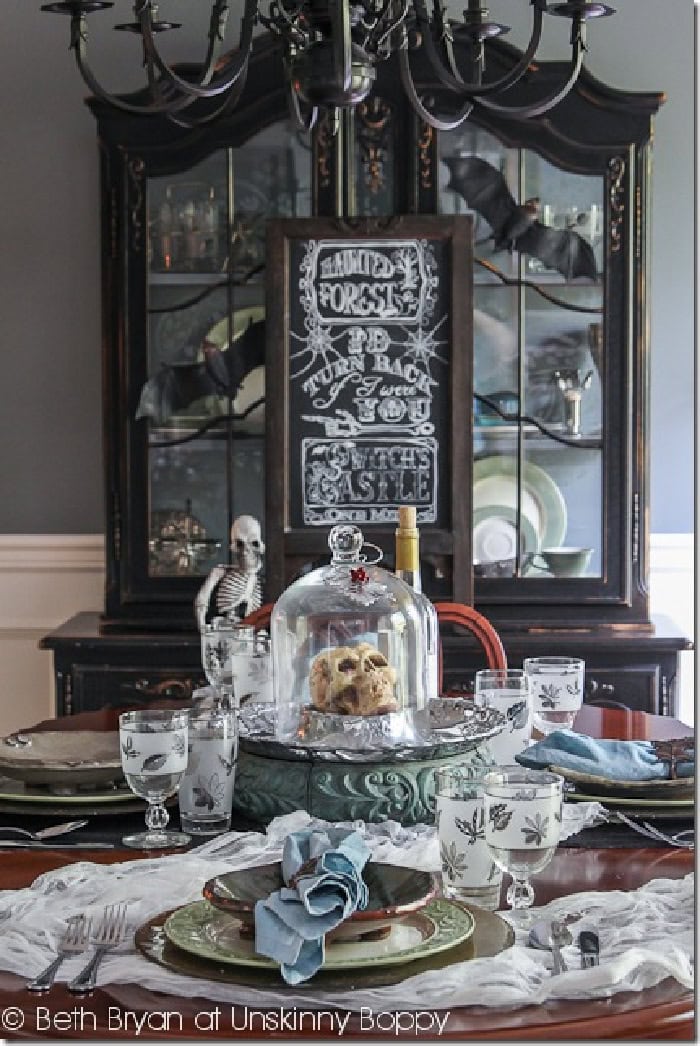 A table setting for Halloween done with a scary Halloween centerpiece featuring skulls in a bird cage.