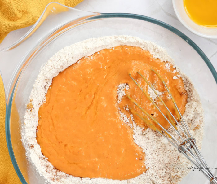 Mixing wet pumpkin pancake ingredients into the dry ingredients with a whisk.