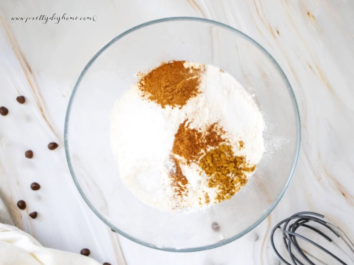 A large bowl with flour, baking powder, pumpkin spices and other dry ingredients for making pumpkin cookies. You can see the topof a wisk in the lower tight hand corner.