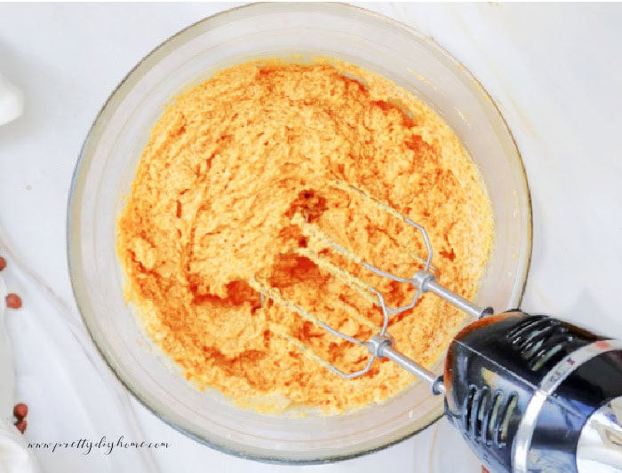 A large bowl of pumpkin cookie batter being mixed with a mixer. The counter the bowl is on is marble.