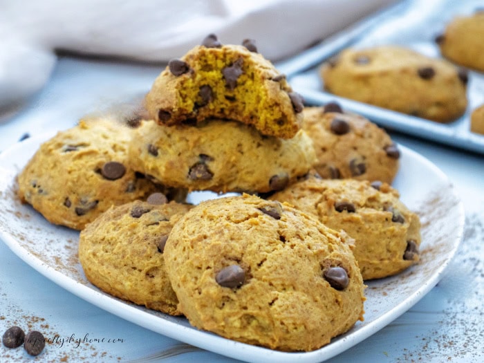 A large plate of homemade pumpkin cookies, in a casual pile. The cookies are golden brown thick and chewy and are filled with lots of chocolate chips.