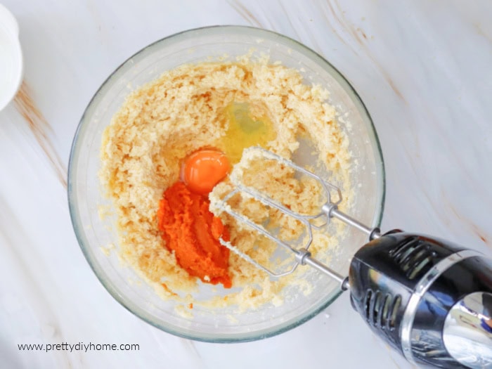 A large bowl sitting on a marble counter. The bowl is filled with the wet ingredients for a pumpkin cookie recipe.