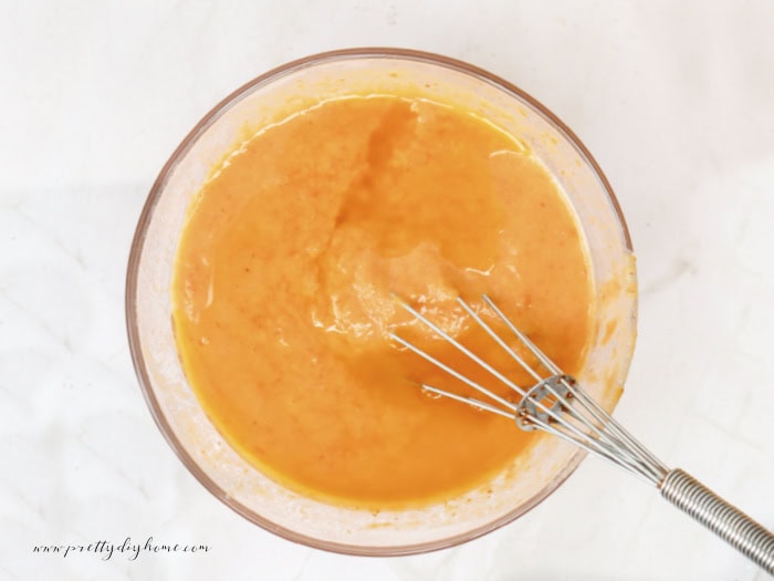 A clear glass bowl filled with soft orange colored pumpkin mixture of wet ingredients for pancakes.