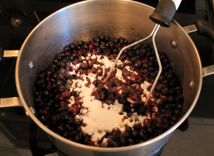 Saskatoon berries being mashed in a large pot, with certo and lemon juice.