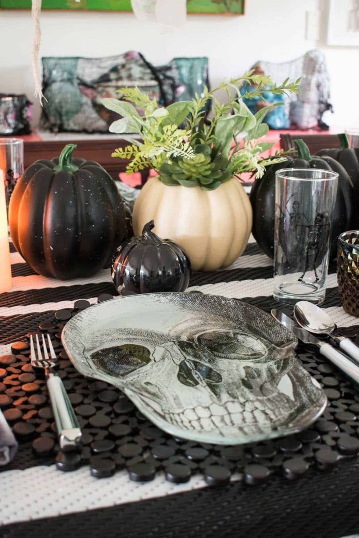 A simple Halloween centerpiece with white and black pumpkins in a table setting.  The Halloween tablesetting is elaborate with very spooky skeleton placemats.