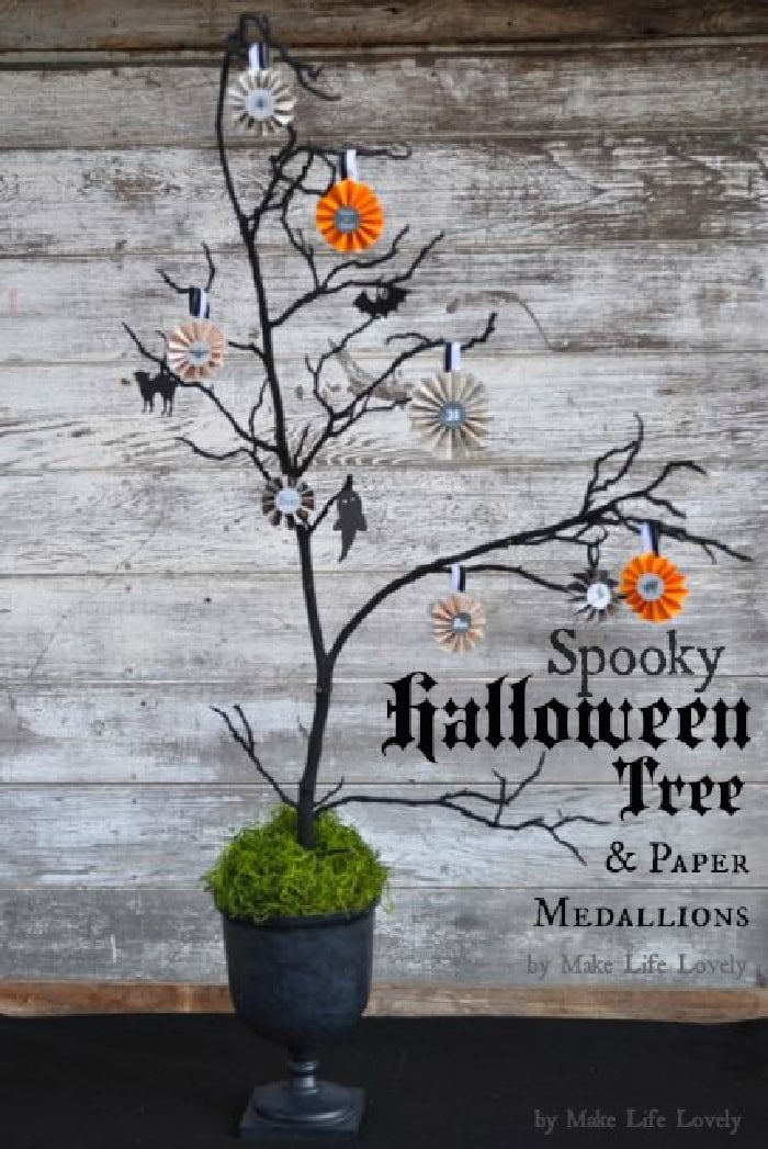 A tree branch painted black, in a large flower pot painted black as well. The spooky branches of the tree decoration are decorated with colorful Halloween themed paper medallions.