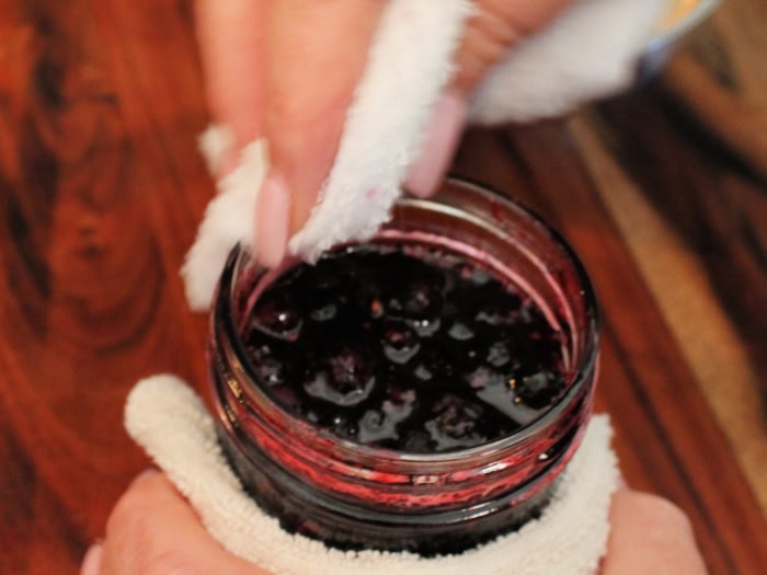 Wiping the rim of a jar of saskatoon berry jam before sealing it.