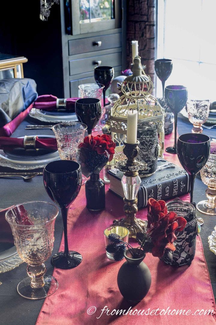 A black skeleton head Halloween centerpiece, sitting in a bird cage. The centerpiece is part of a large red and gold table setting for Halloween.