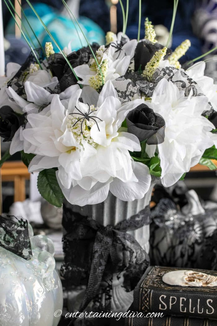 The centerpiece for an elegant black white and gold Halloween tablescape . It has white flowers, black roses, a beautiful spell book and lace.  Its very feminine, pretty and spooky.