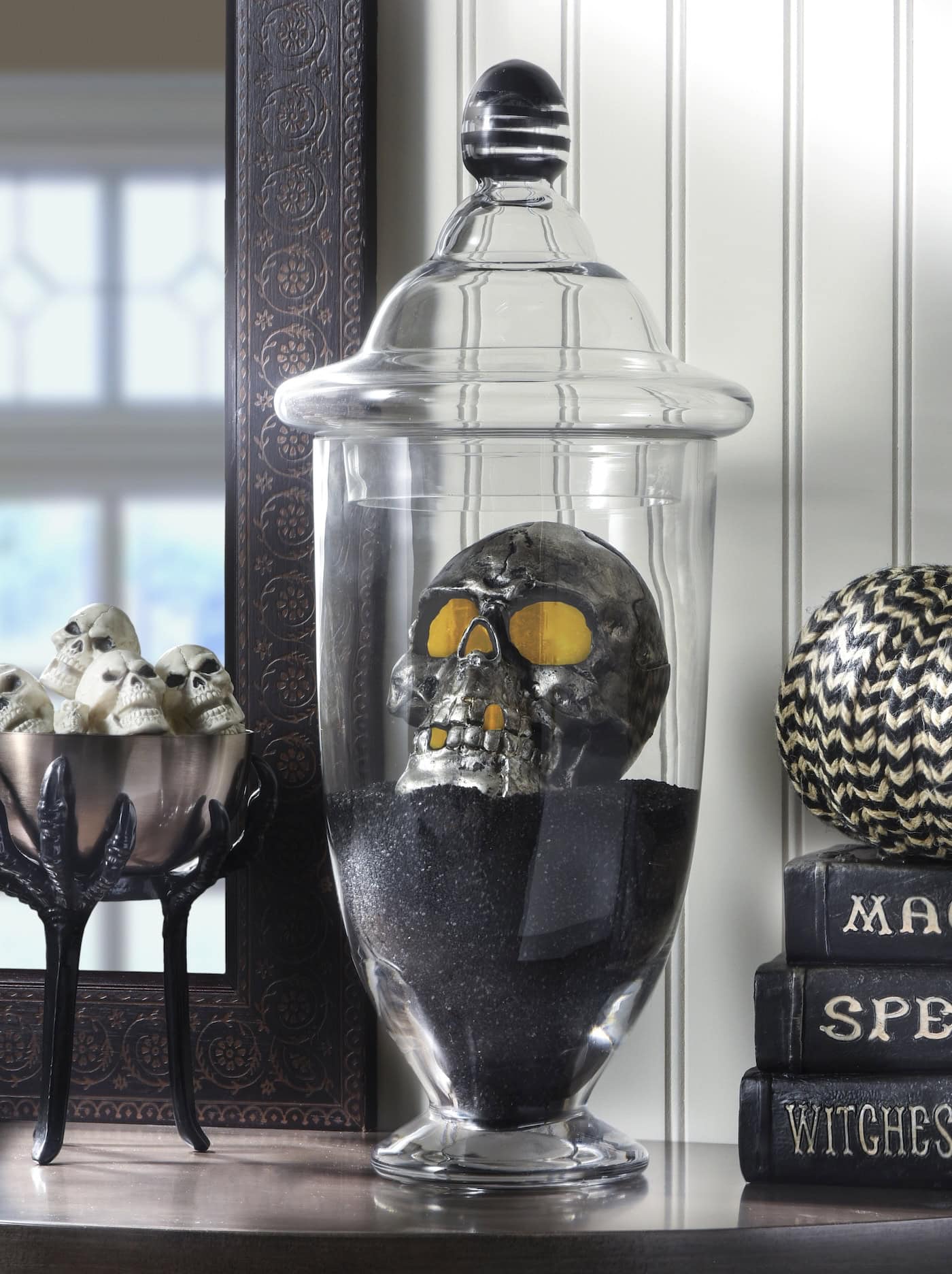 A large apothecary jar filled with sparkling black sand and a black skeleton.