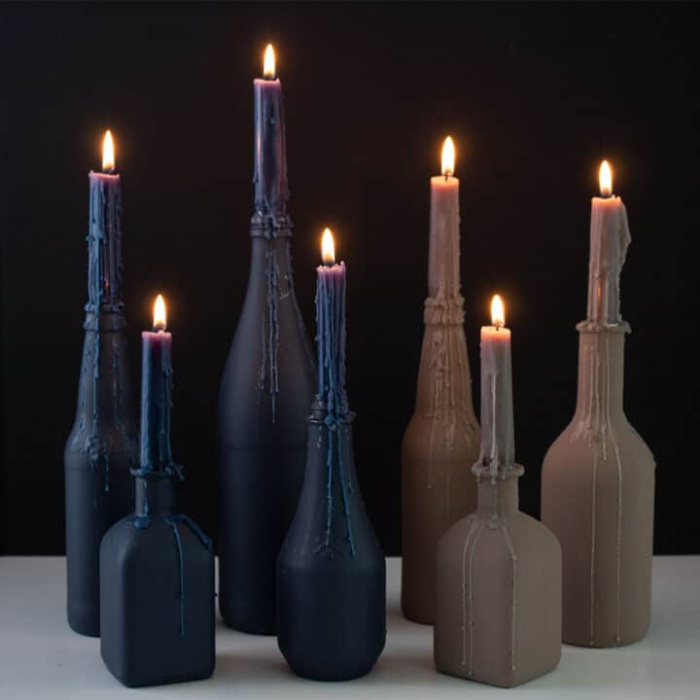 Six candles painted for Halloween in dark blue, and other dark brown.  Each bottle holds a dripping tapered candle.  The effect is both elegant and creepy.