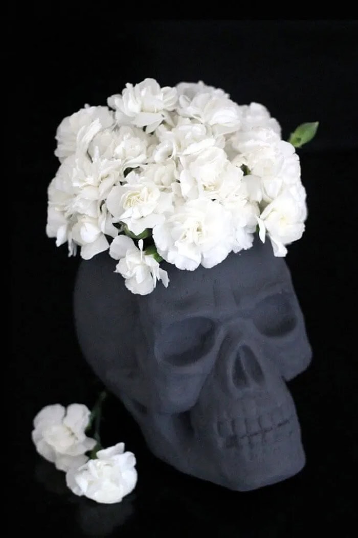 A black skull used as a vase for white flowers for an easy and elegant Halloween centerpiece.
