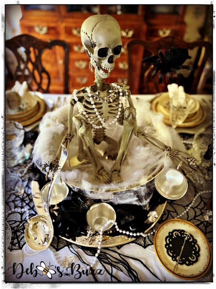 A gothic scary Halloween tablesetting. The centerpiece is a large skeleton with jewelry. The color scheme is an elegant black and gold.