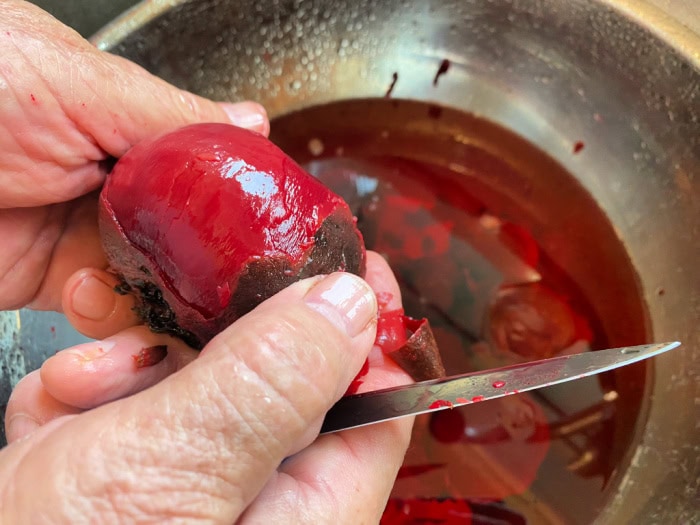 Removing the skins off of fresh cooked beets while working under cool water.  You can see a large stainless bowl underneath to catch the beet peels.