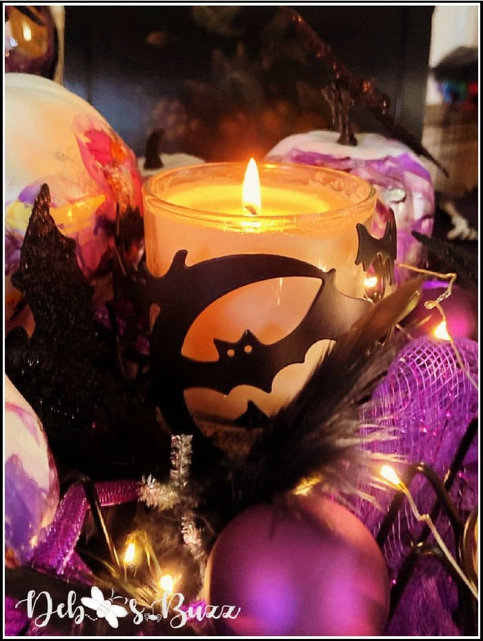 A purple and black Halloween table centerpiece featuring a candle and bats.