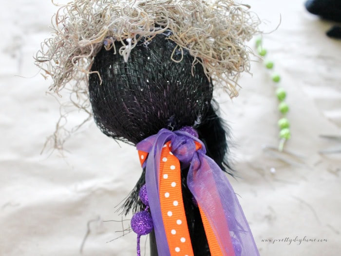 A DIY Halloween witch wand with bright purple and orange ribbons being tied to it.