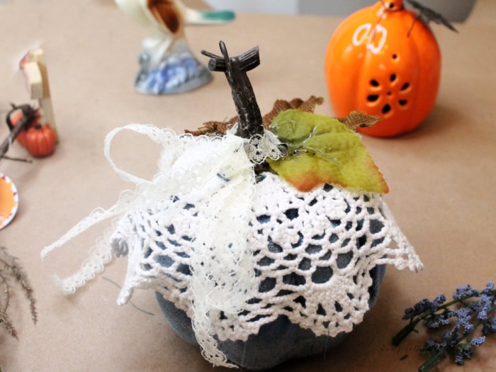 Tying a ribbon to a doily covered blue dollar tree pumpkin fall craft.