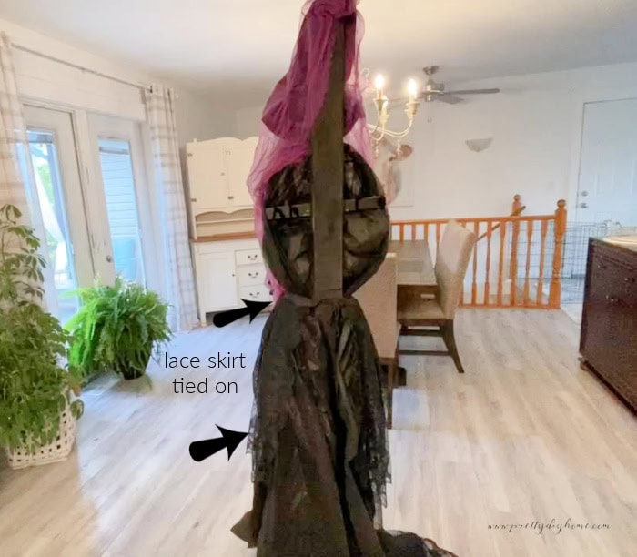 The back an an upcycled hanging with tied to a standing pole that shows, you can see a pretty lace skirt and fuller long skirt but she needs a cape to hie the wood "backbone"