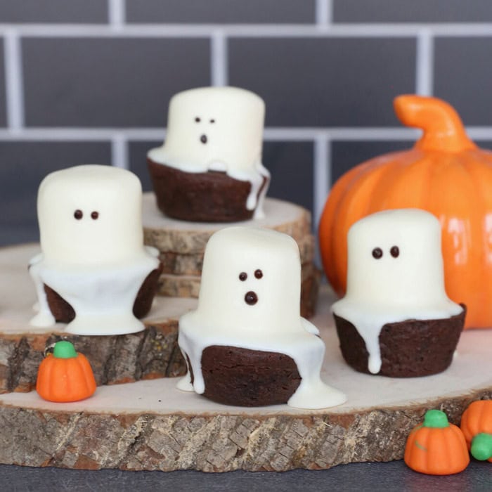 Four fun Halloween brownie ghosts with cute faces sitting on a wood slice.