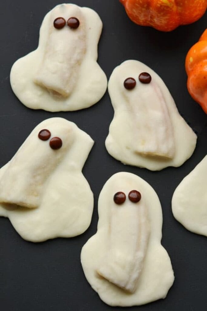 Bananas covered with large coating of white chocolate that swirls around the bottom  into ghost shapes.  The bananas are then decorated with chocolate chip faces ato turn into adorable ghost treats.