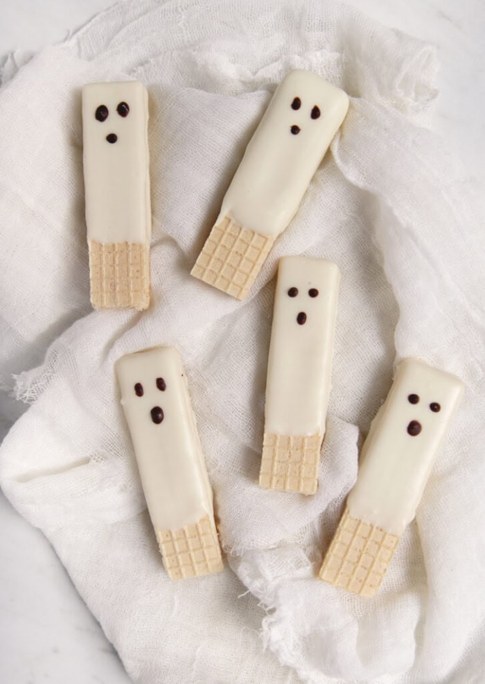 Ghost cookie wafers in white chocolate with little dots for eyues and noses.  They are adorable cookies on a white background.