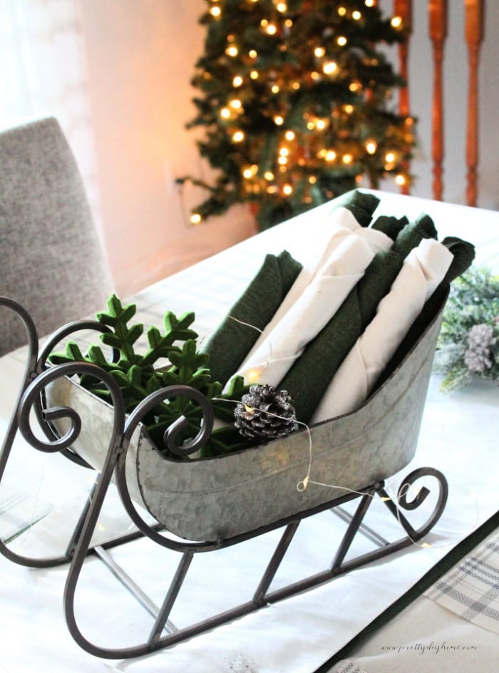 Nicely folded napkins in a galvanized sleigh sitting on a Christmas table.