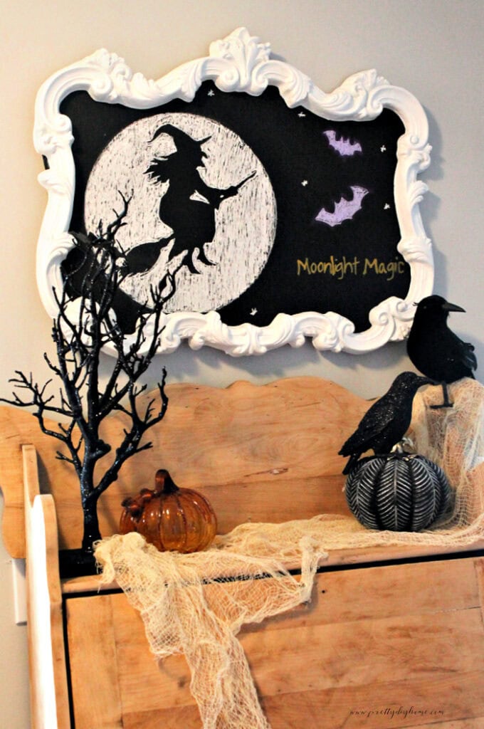 DIY Halloween DIY decor idea with a witch and two bats. Its hung above an antique cabinet thats a ligight gol and drecorated with sparkly black Halloween tree and black crows