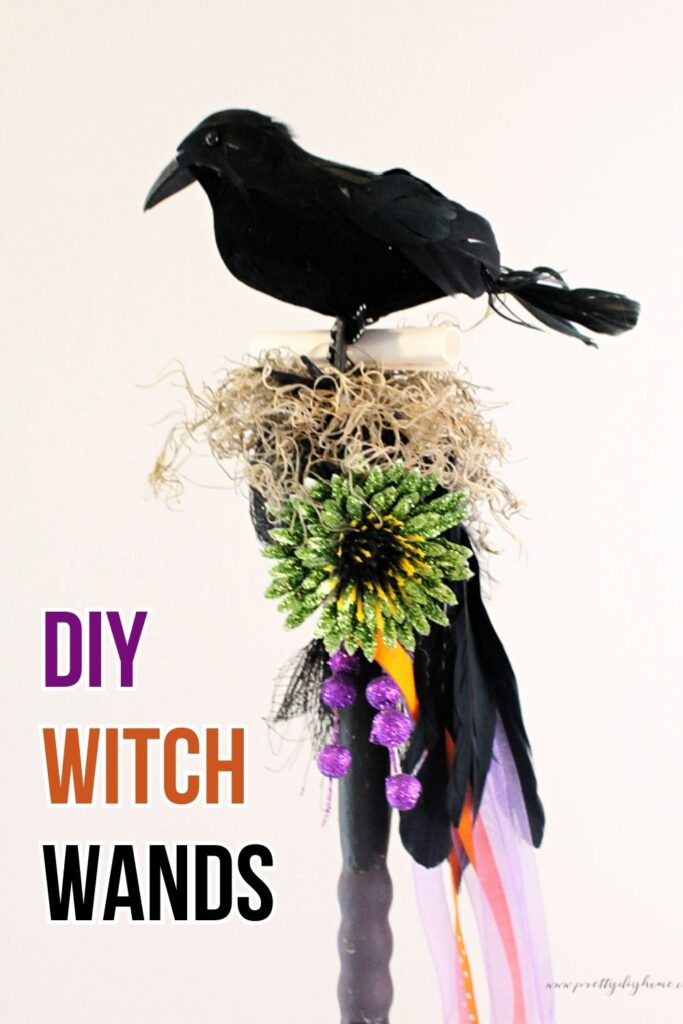 A sparkling witch wand with a black raven on top of a raffia nest, bright neon green Halloween flower and cascading feathers and ribbons in orange, purple, and black.