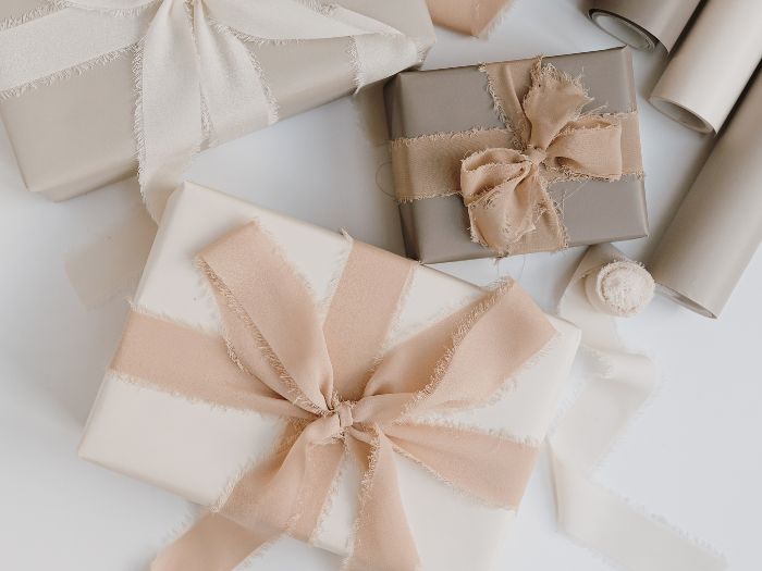 Neutral and blush Christmas gifts wrapped with soft fabric ribbon bows, elegant feminine gift wrapping style.
