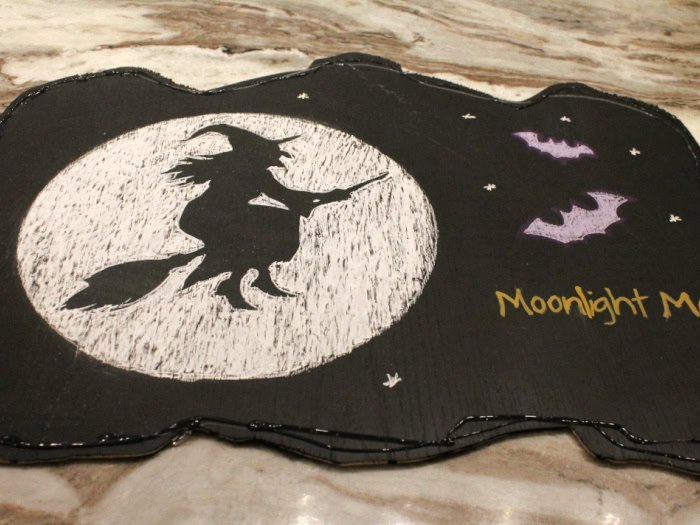 Finished halloween chalkboard art with a witch in the moon, two purple bars and wording that says moonlight magic. The chalkboard is outlined in a strip of hot glue and E6000 glue for attaching a upcycled frame to it.