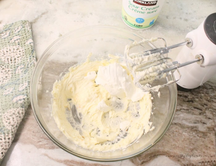 Mixing sour cream into well beaten butter using an electric mixer. The first step to making a pumpkin loaf recipe with sour cream.