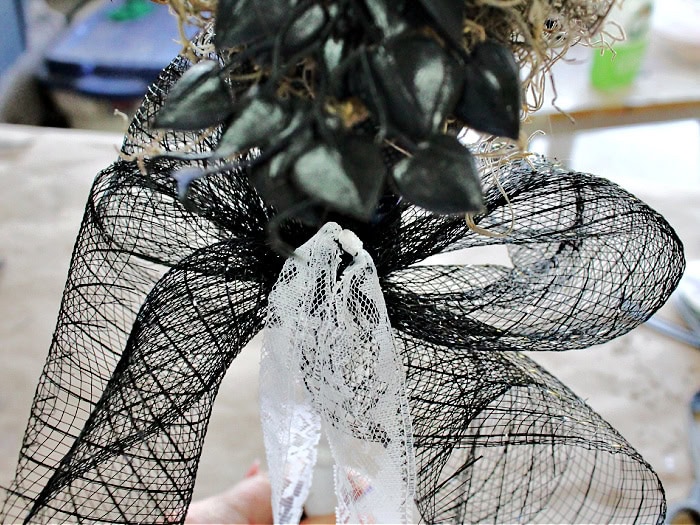 A close up of a mesh ribbon and a lace ribbon being tied to the underside of a Halloween witch wand.
