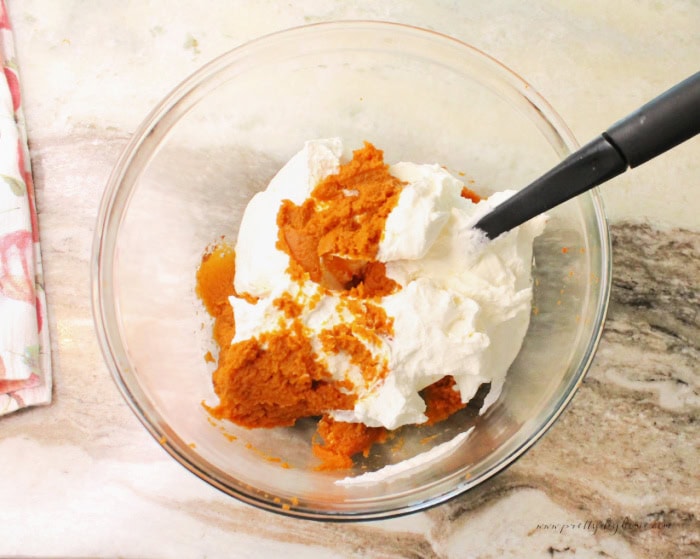 Mixing the wet ingredients for a pumpkin mousse together. Pumpkin puree, spices, and already whipped whipping cream being folded together with a spatula.