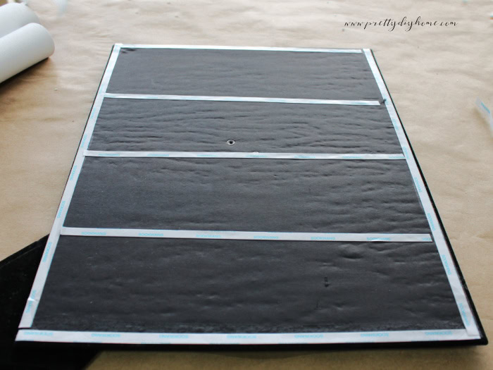 Adding doubled sided tape to the front of a frame backing. The tape is around all the outside edges, and in three strips across as well.