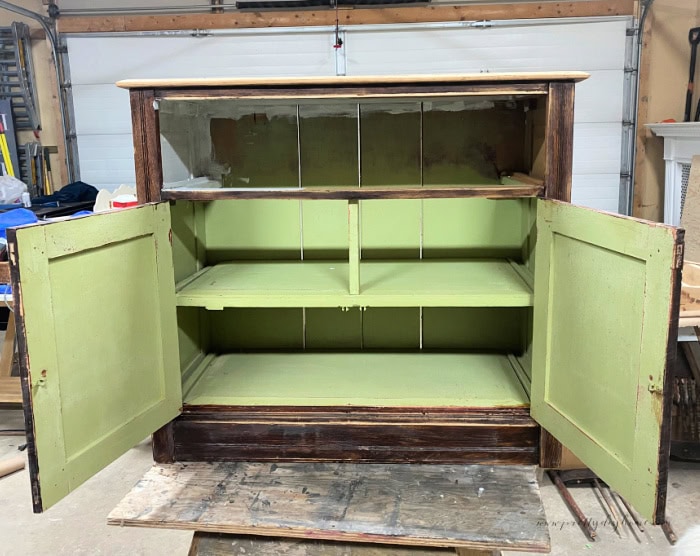 The interior of an antique solid wood cabinet painted a bright neon green in parts, with swatches of white paint along parts of the inside as well as unpainted areas.