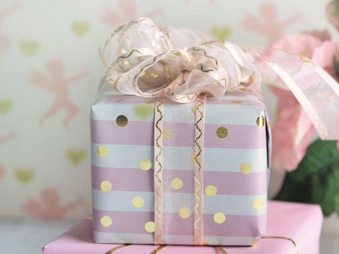 Pink and gold Christmas gift wrapped with striped and polka dot paper and a sheer ribbon bow, playful wrapping idea for little girls.