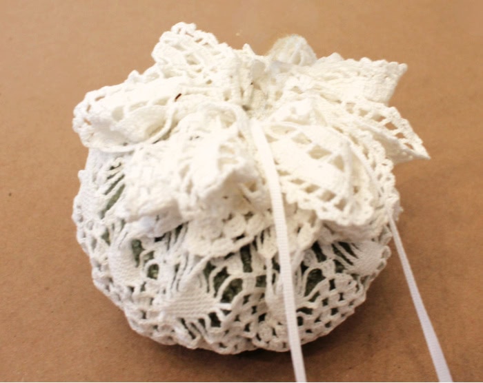 A vintage doily is pulled tight around a light green Dollar Tree pumpkin and then tied with a pretty white bow.