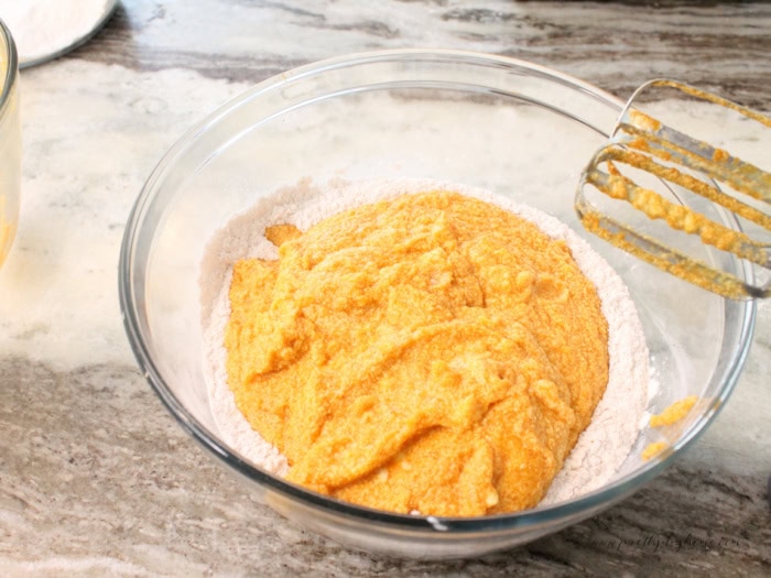 Wet ingredients being added to the middle of a bowl of dry ingredients for a pumpkin bread with sour cream recipe.