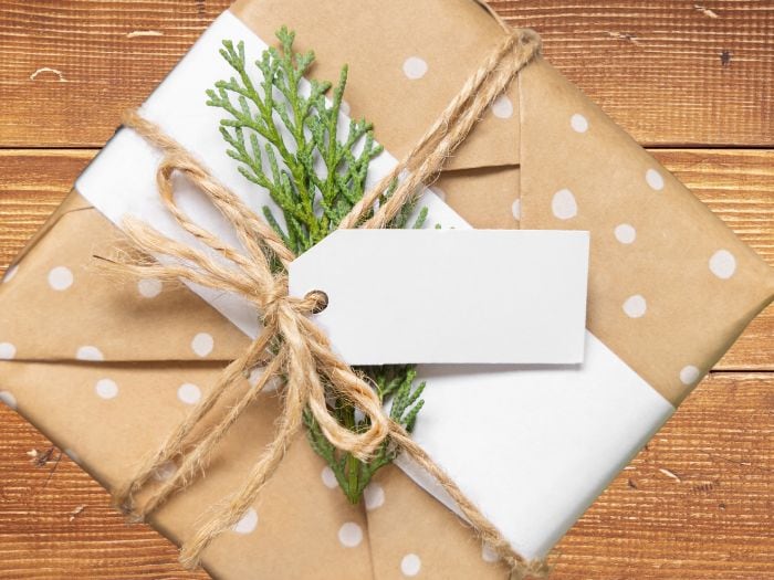 Rustic Christmas gift wrapped in kraft paper with white polka dots, twine bow, greenery, and a blank gift tag