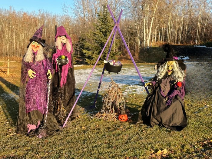 Three diy witch Halloween props sitting around a diy witches cauldron as front yard Halloween decorations,