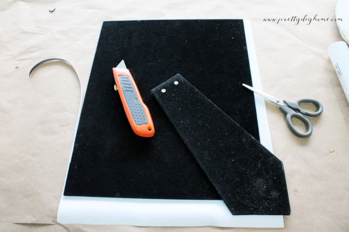A canvas laying flat with the back of the frame over top.  The frame will be used as a template for cutting to size.  The cutting knife and the scissors are laying nearby.
