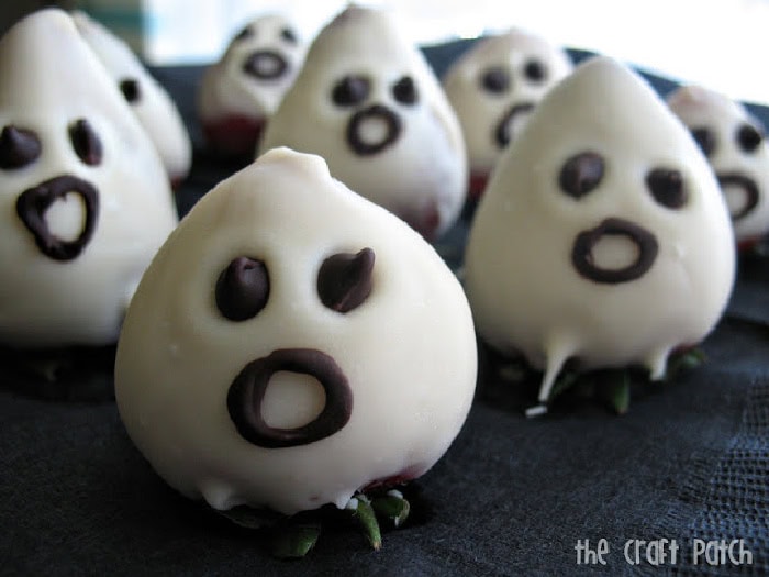 Several white chocolate covered strawberries that look like little ghosts with chocolate chip eyes and circular piped on chocolate mouths.