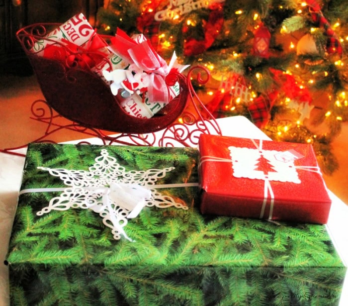 two Christmas presents one wrapped in red another in green. Both presents have elaborate flat cutout embellishments on top as an example of how to wrap gifts for shipping ar Christmas.