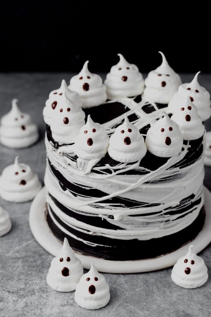 A large chocolate layer cake made with black cocoa.  The cake is decorated with lots of little meringue ghosts and a meringue spiderweb around the outside of the cake.