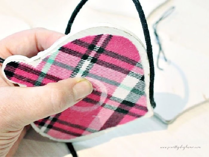 Wrapping black cord around the outside edge of a pink flannel covered Christmas tree ornament to finish the DIY decoration.