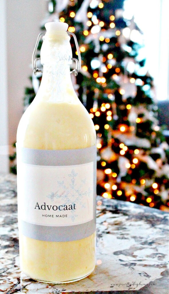 Bottle of homemade advocaat with a blue snowflake label in front of a twinkling Christmas tree.