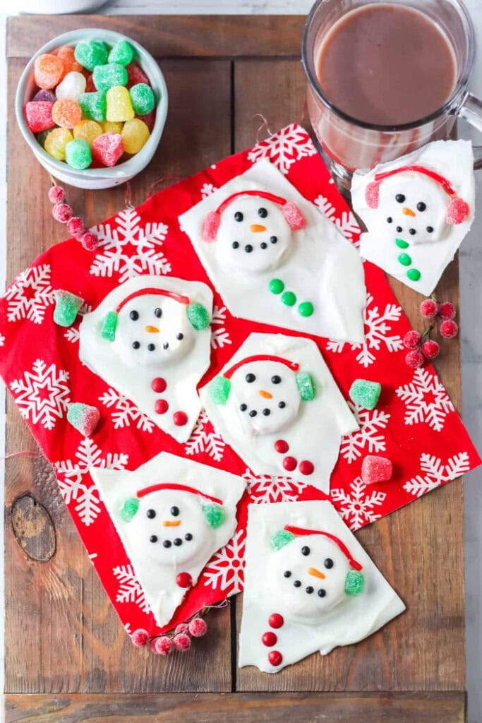 Oreo Christmas bark recipe where the whjite chocolate is poured over the cookie but look like melteed snowmen and the whole oreo cookie forms the backdrop for the head of the snow man. Each melted snowman Christmas candy is decorated with gumdrop and twizzler ear muffs, black icing eyes and little orange icing noses.